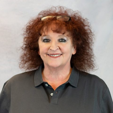 Lächelnde Frau mit lockigem, rotem Haar, trägt ein graues Polo-Shirt.