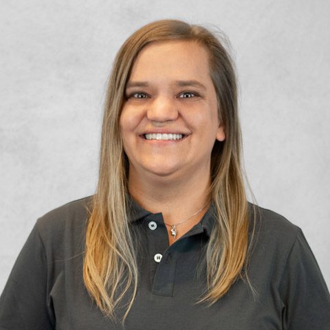 Lächelnde Frau mit langen, blonden Haaren in einem grauen Hintergrund.