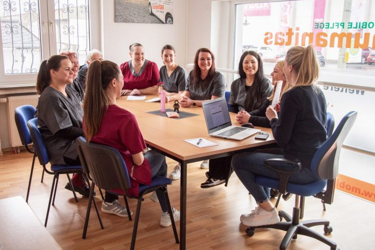 Fröhliches Teammeeting der mobilen Pflege Humanitas  an einem Tisch mit Laptops und Notizen.