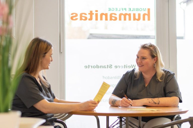 Zwei Frauen sitzen an einem Tisch in einem Büro der mobilen Pflege Humanitas und diskutieren über Unterlagen.