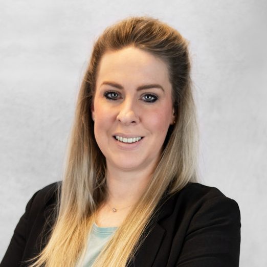 Porträt einer lächelnden Frau mit langen, blonden Haaren und schwarzer Jacke.