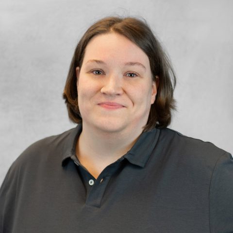 Person mit kurzer brauner Haarfrisur, die ein dunkles Polohemd trägt.