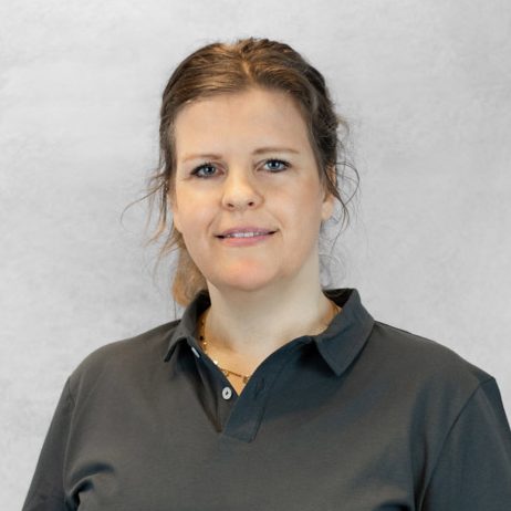 Eine Frau mit langen, braunen Haaren trägt ein schwarzes Polo-Shirt und lächelt.